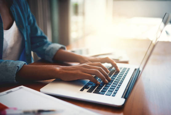 Close-up of a woman's hands typing on a laptop at home.
